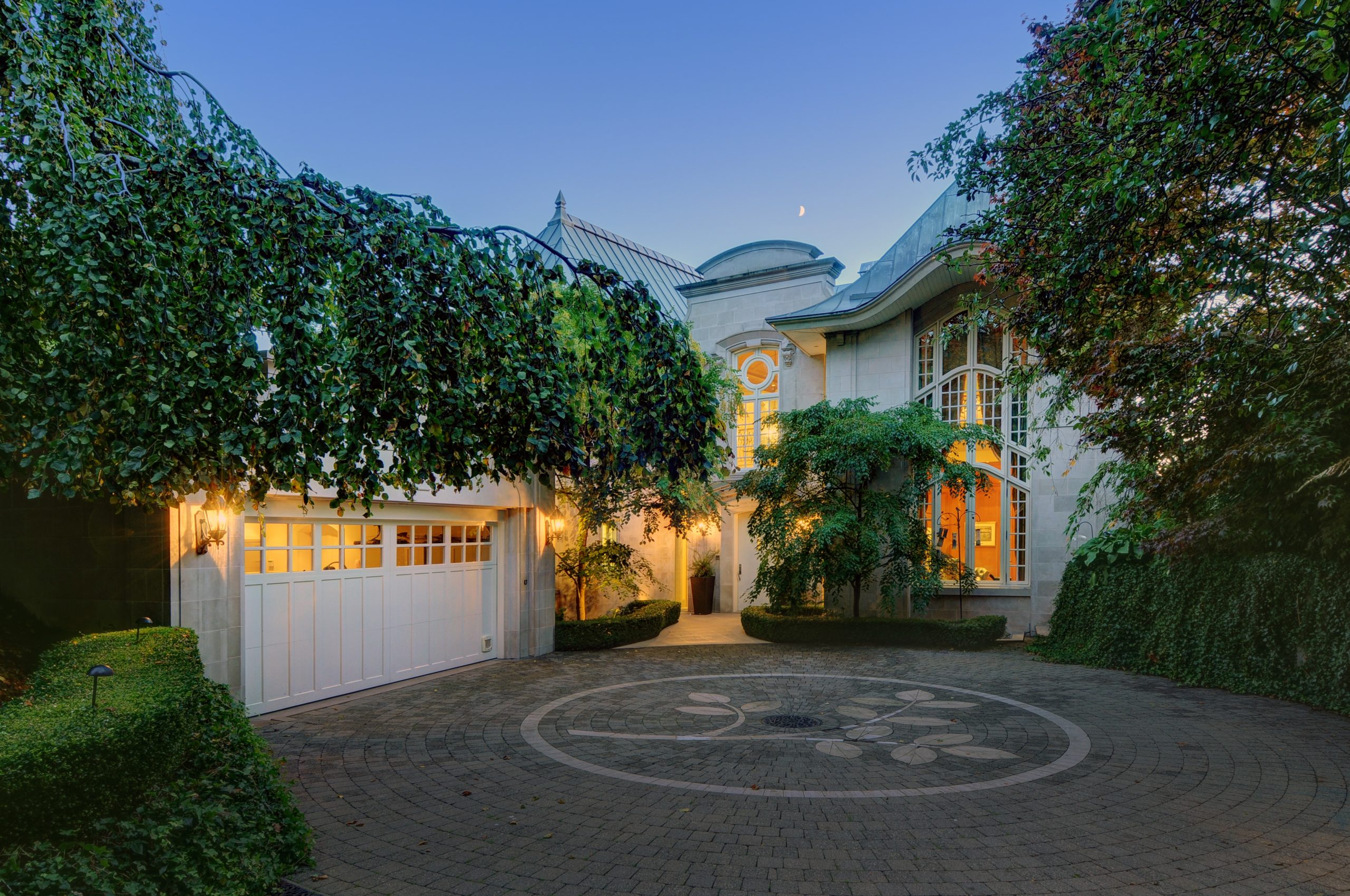 Elegant house with large windows, ivy-covered walls, circular driveway, and warm exterior lights at dusk—crafted by a trusted BC General Contractor for timeless curb appeal.