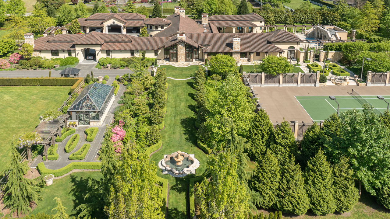 Aerial view of a large estate in British Columbia with gardens, a tennis court, and a greenhouse surrounded by trees.