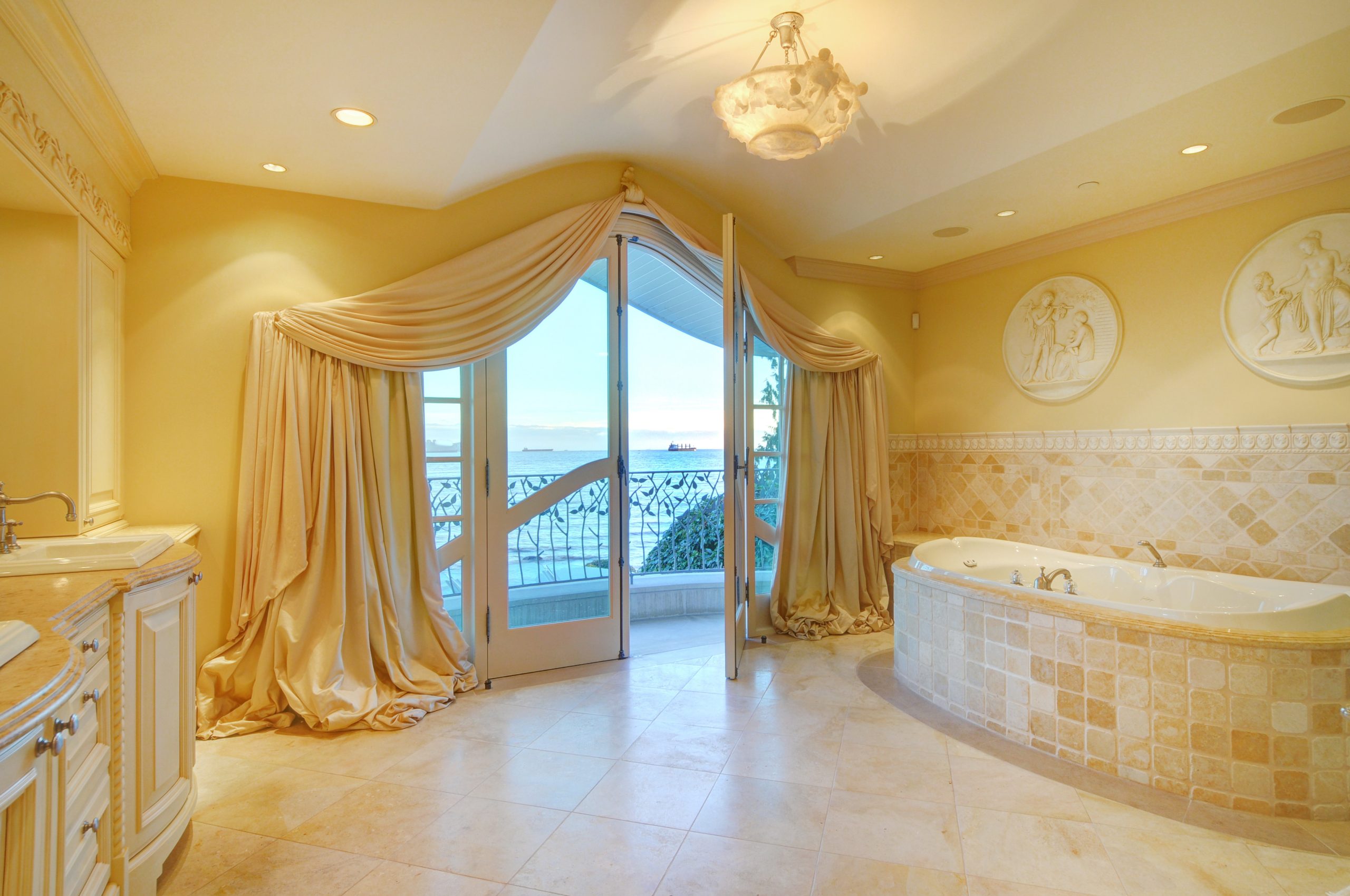 Luxurious bathroom with draped curtains, a large tub, and doors opening to a balcony with an ocean view—an elegant touch found in Vancouver’s finest custom homes.
