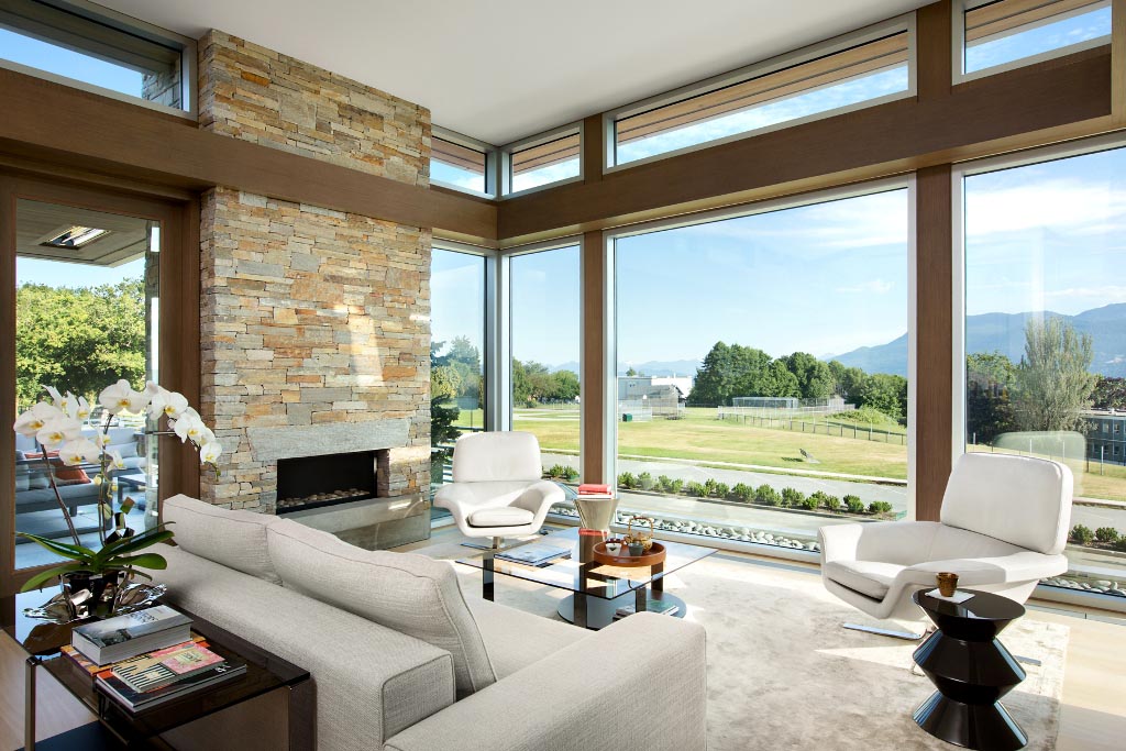 Living room in Vancouver, BC, with large windows, light furniture, and a stone fireplace overlooking a scenic outdoor view—perfect for your company to relax or entertain.