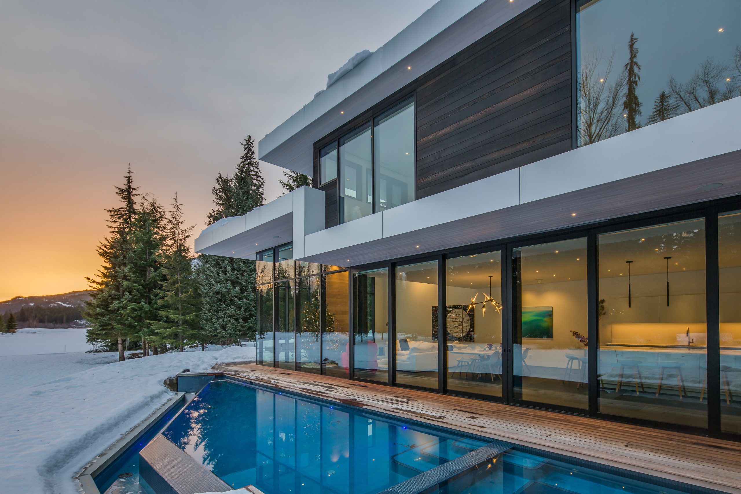 House with large windows, outdoor pool, and snowy landscape at sunset—expertly crafted by a BC general contractor.