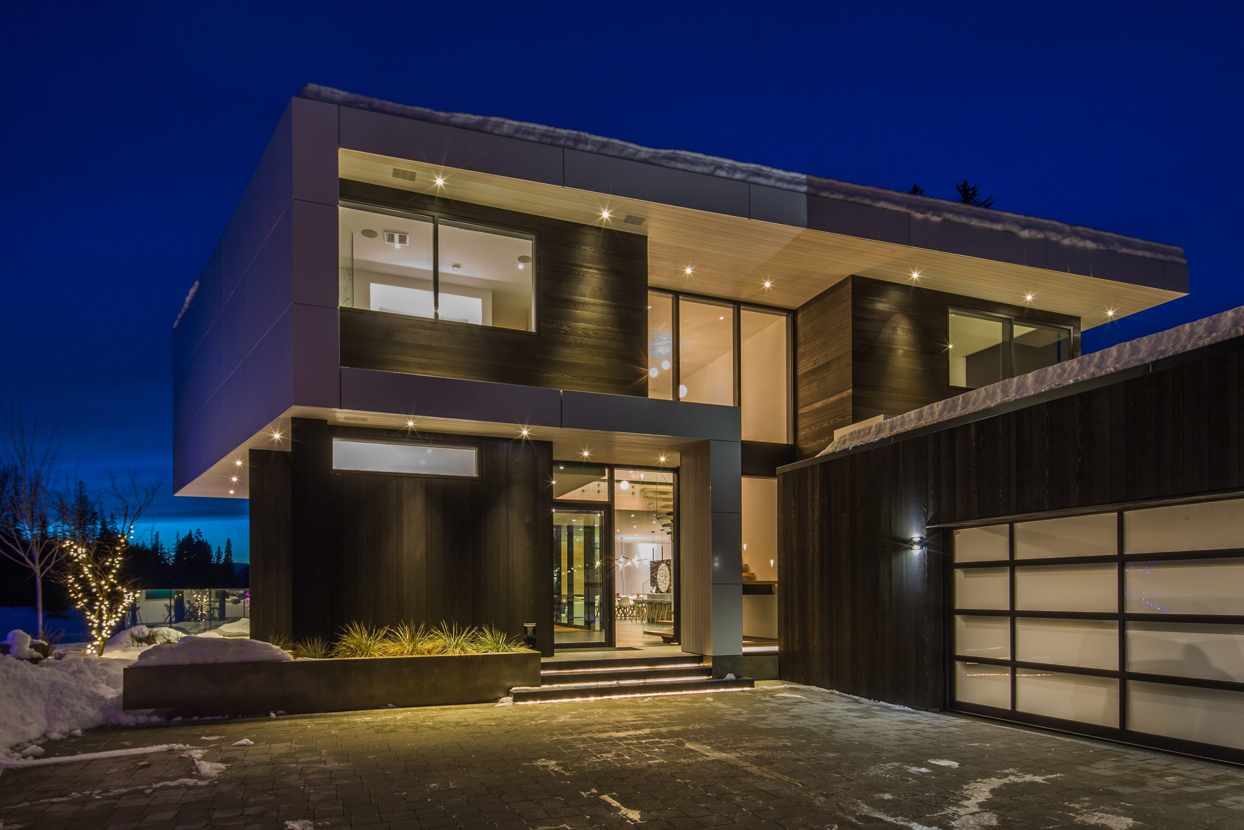 Two-story custom home with large windows, striking exterior lights, and snow-covered ground at night—a stunning example of contemporary architecture often seen in British Columbia.