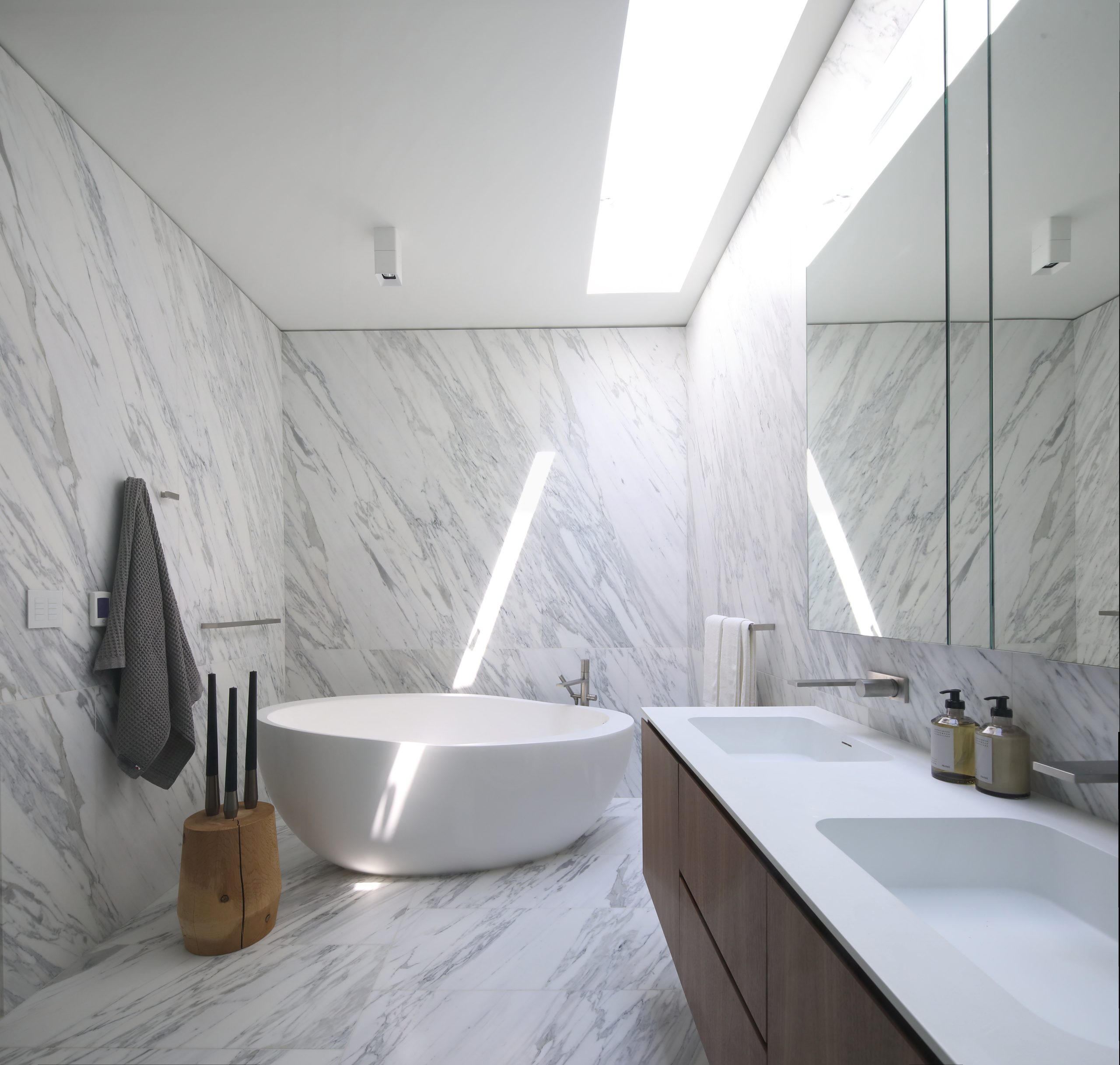 Bathroom with marble walls, a freestanding tub, double sinks, and natural light from skylights highlights exquisite architecture found in custom homes throughout Vancouver.