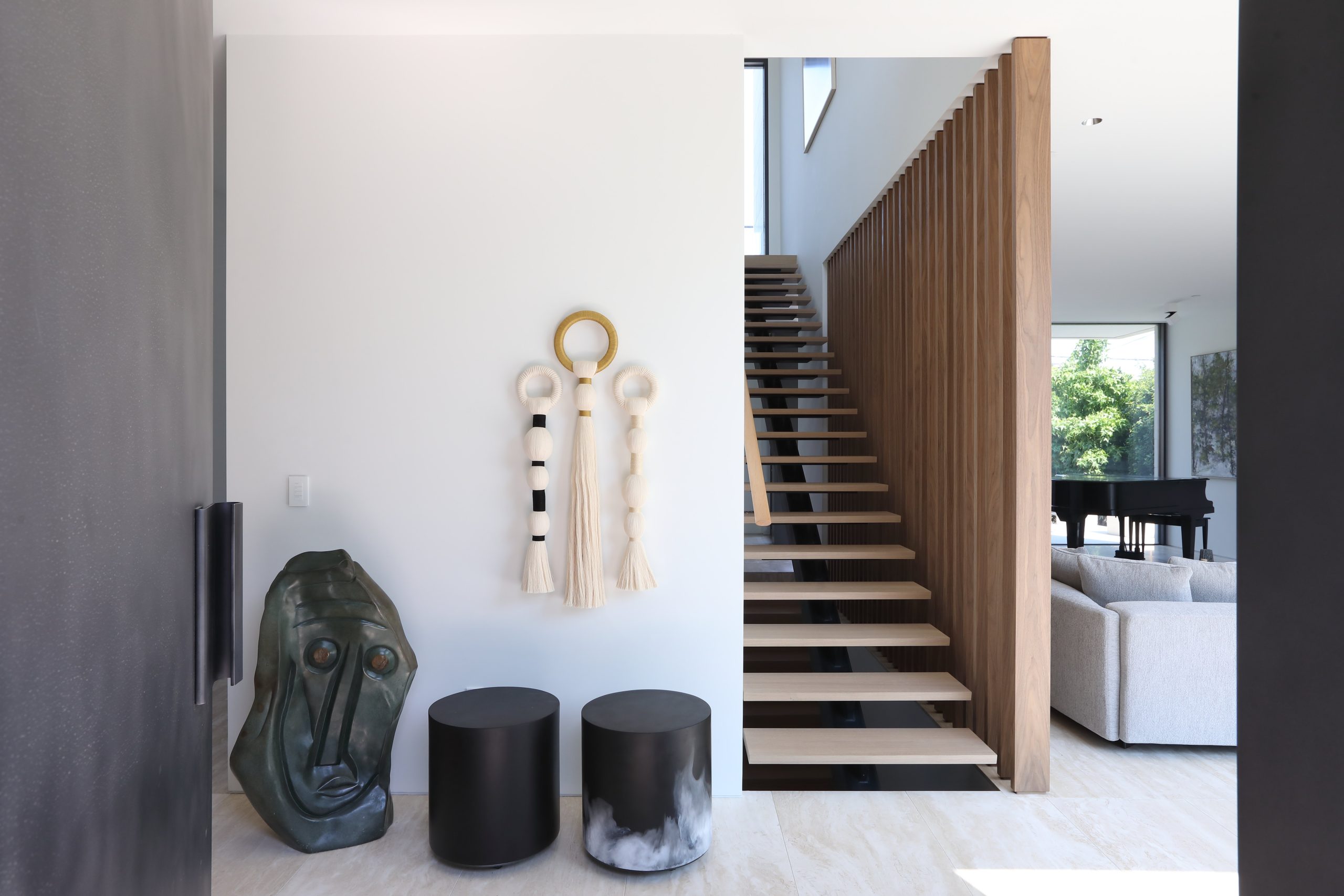 Entryway with floating wood stairs, showcasing Vancouver architecture, abstract wall art, two round stools, and a sculptural face piece that elevates the quality of the space.