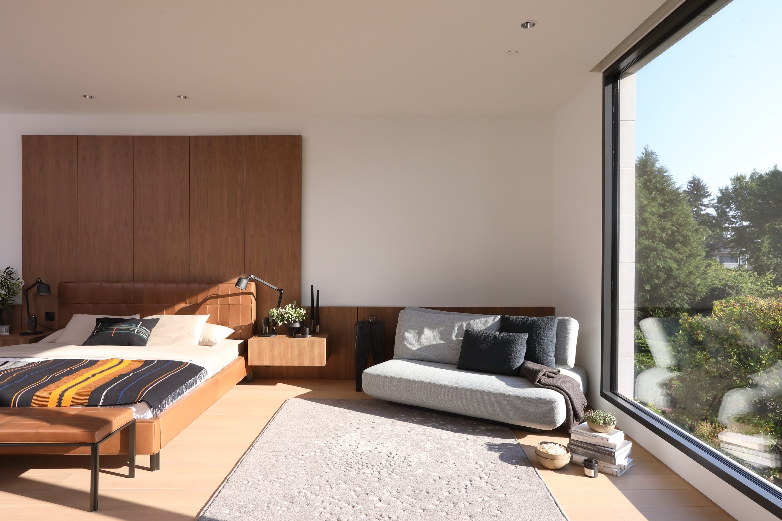 Bedroom in Vancouver with large window, wooden accents, a bed, sofa, and views of greenery—expertly designed by a reputable company in custom homes.