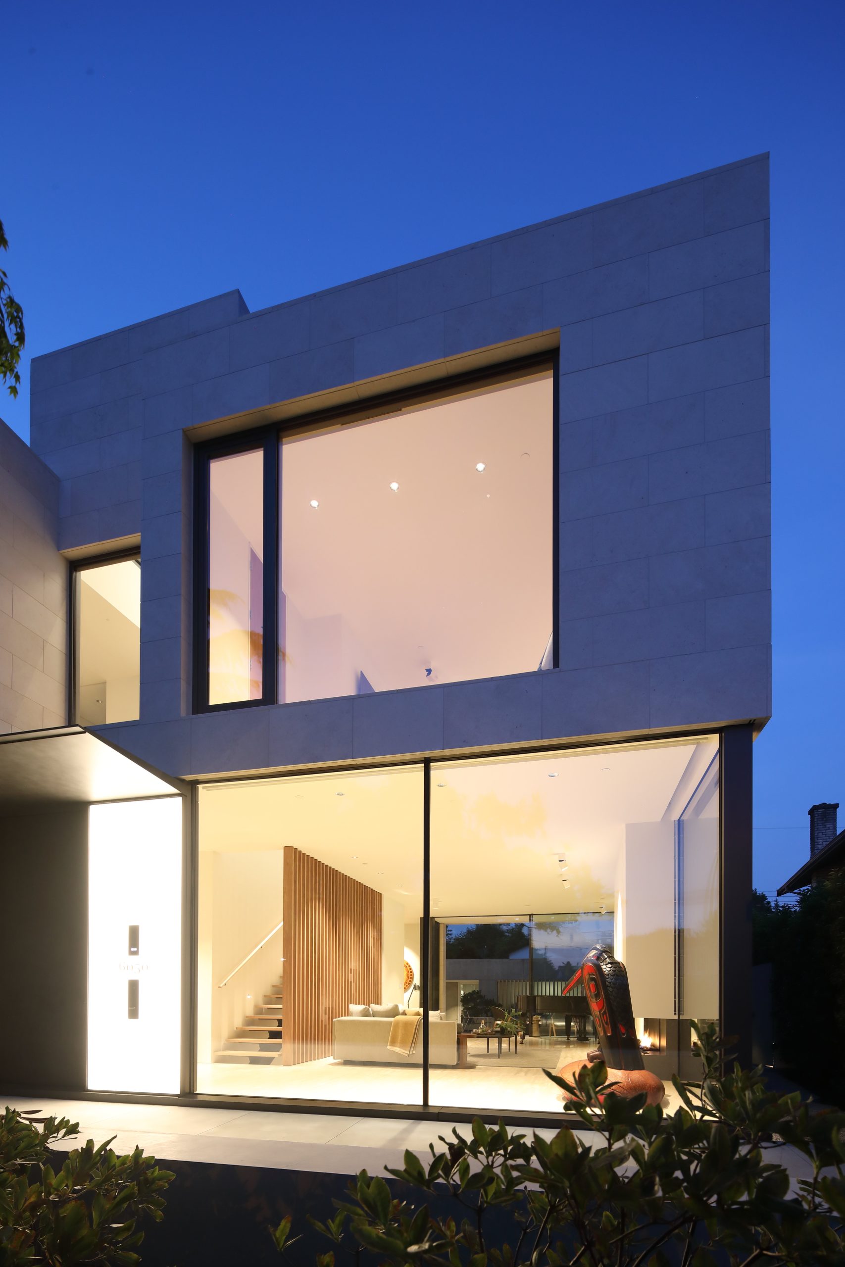 Two-story house with large glass windows, warmly lit interior, and minimalist architecture at dusk—an elegant Vancouver residence crafted by a reputable constriction company