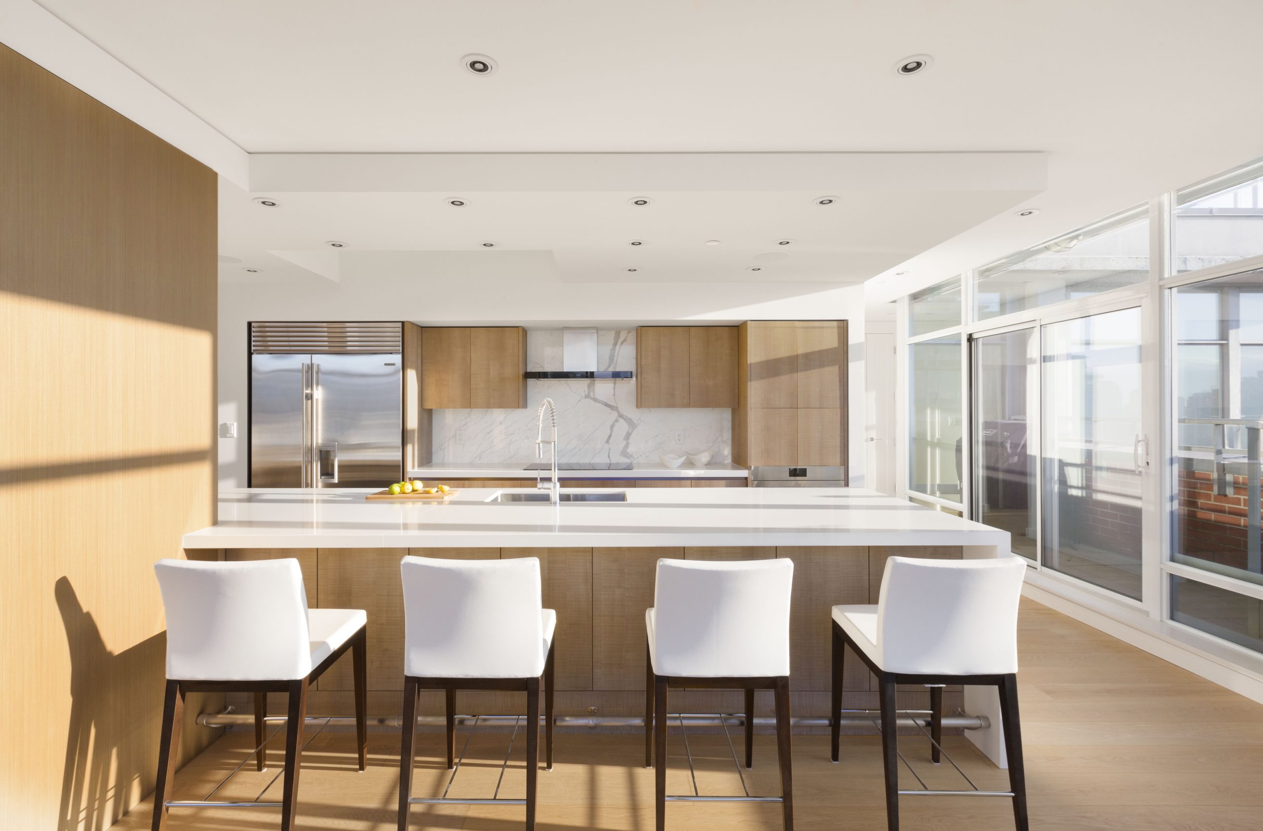 Kitchen with white countertops, wood cabinets, and four white barstools at a central island—perfect for contemporary Vancouver living.