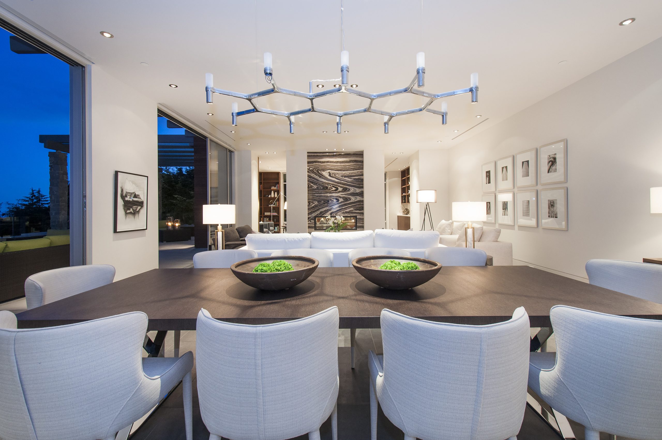 Dining room with a dark table, white chairs, and contemporary lighting, expertly crafted by a BC general contractor, opens to a bright living area.