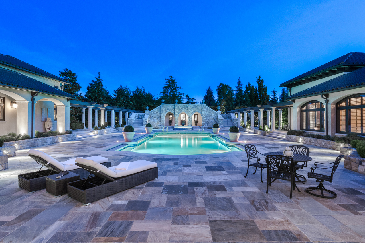 Luxurious poolside patio at dusk with lounge chairs, dining set, and elegant buildings surrounding a lit swimming pool—an inviting retreat inspired by modern BC construction.